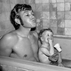 Black-and-white photograph of a dad and two sons in the bath, the dad spitting water out of his mouth