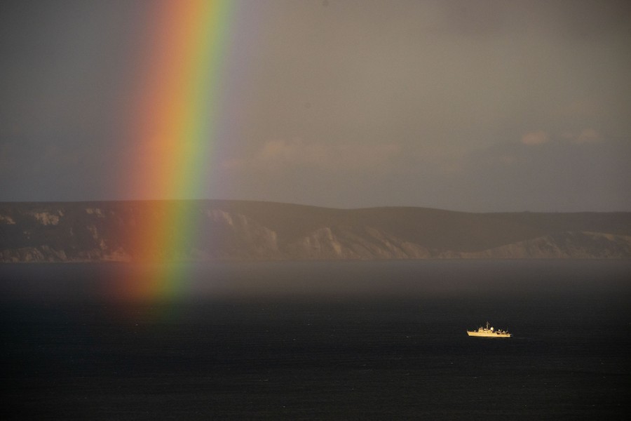A distant view of a ship sailing near the end of a rainbow