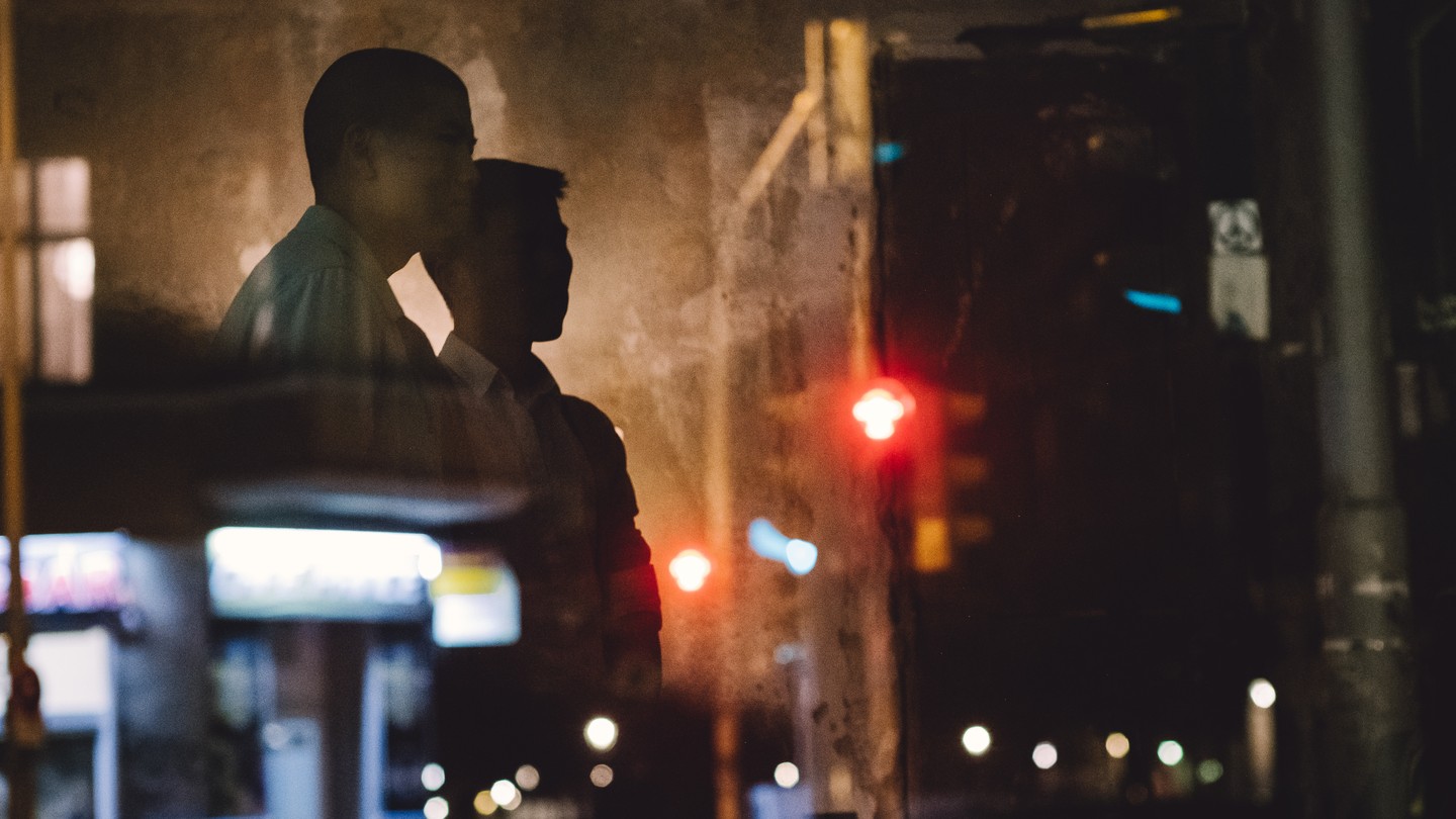 two figures stand at a dark intersection, framed by smoke