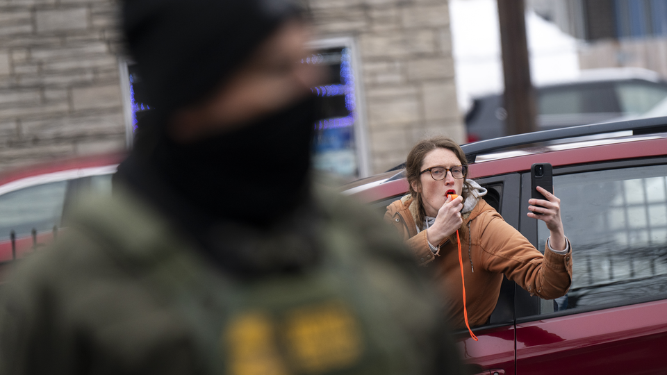 A woman hold a cellphone camera leans out from a car while an out of focus police officer stands in front of her.