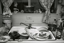 Black-and-white image of a sink overflowing with dirty dishes