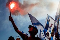 A protester lifting a torch in a crowd of people holding Israeli flags