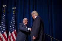 Rudy Giuliani and Trump shake hands in front of two American flags.