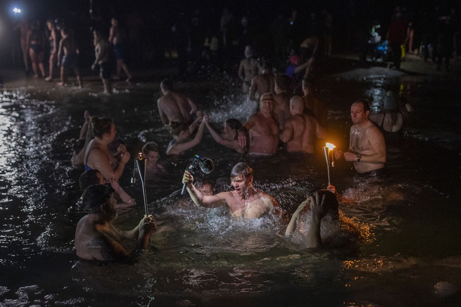 A couple dozen people splash and wade in a lake at night.