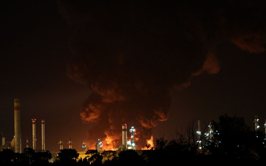Smoke and fire rise above a refinery at night.