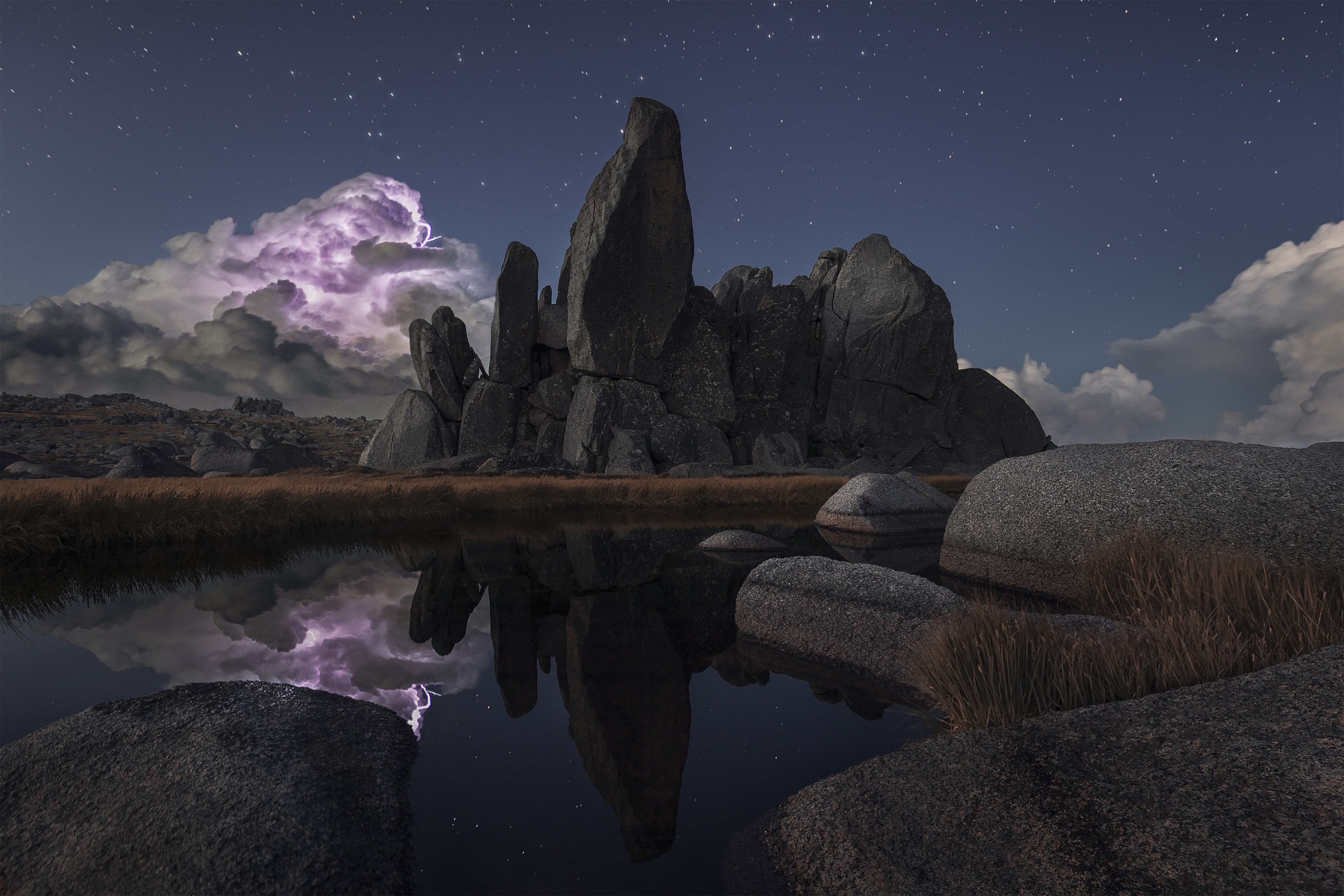 Lightning illuminates a storm cloud behind a large rock formation.