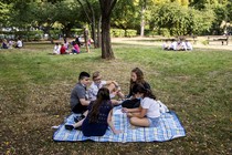 Groups of kids sit spread out on blankets in a park.