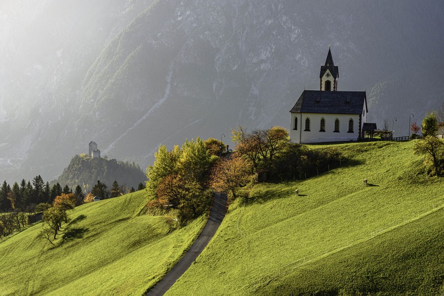 A view of a chapel on a steep mountainside meadow