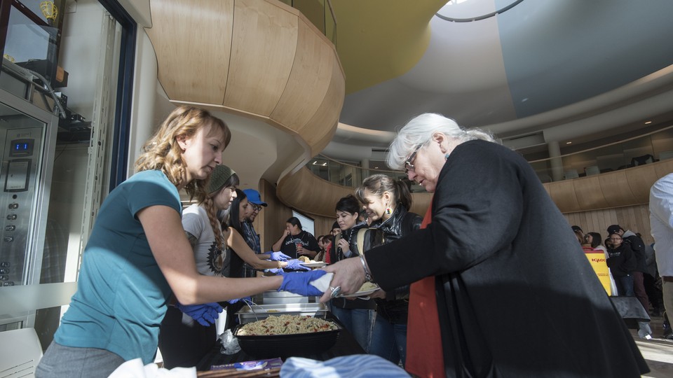 A woman is handed a plate of food. A line of other people is behind her. 