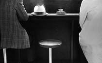 An empty stool in between two people at a dining establishment