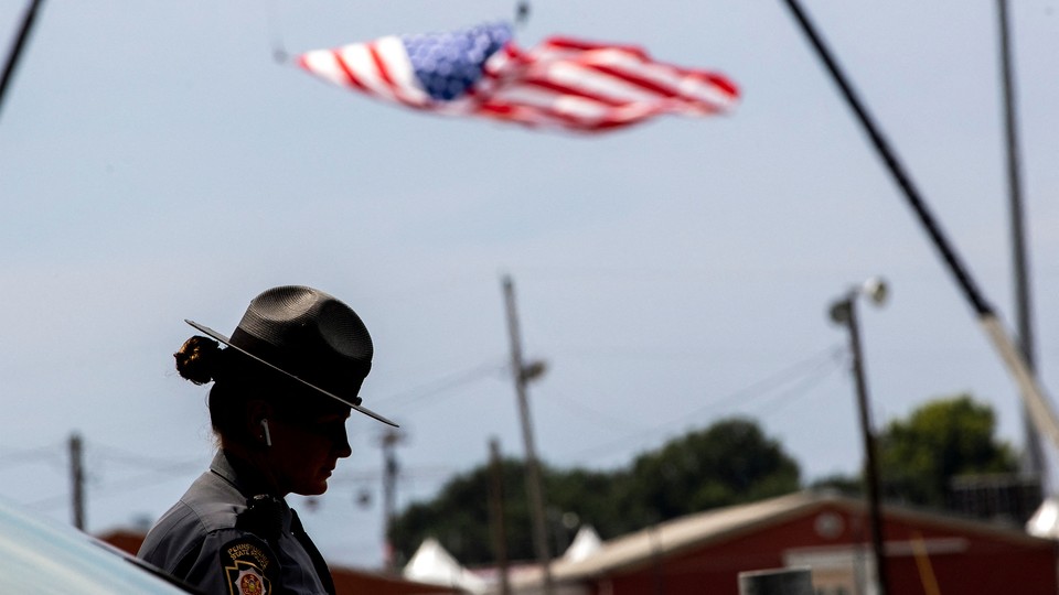A state trooper stands next to a vehicle blocking a road leading to the event grounds in Butler, Pennsylvania.