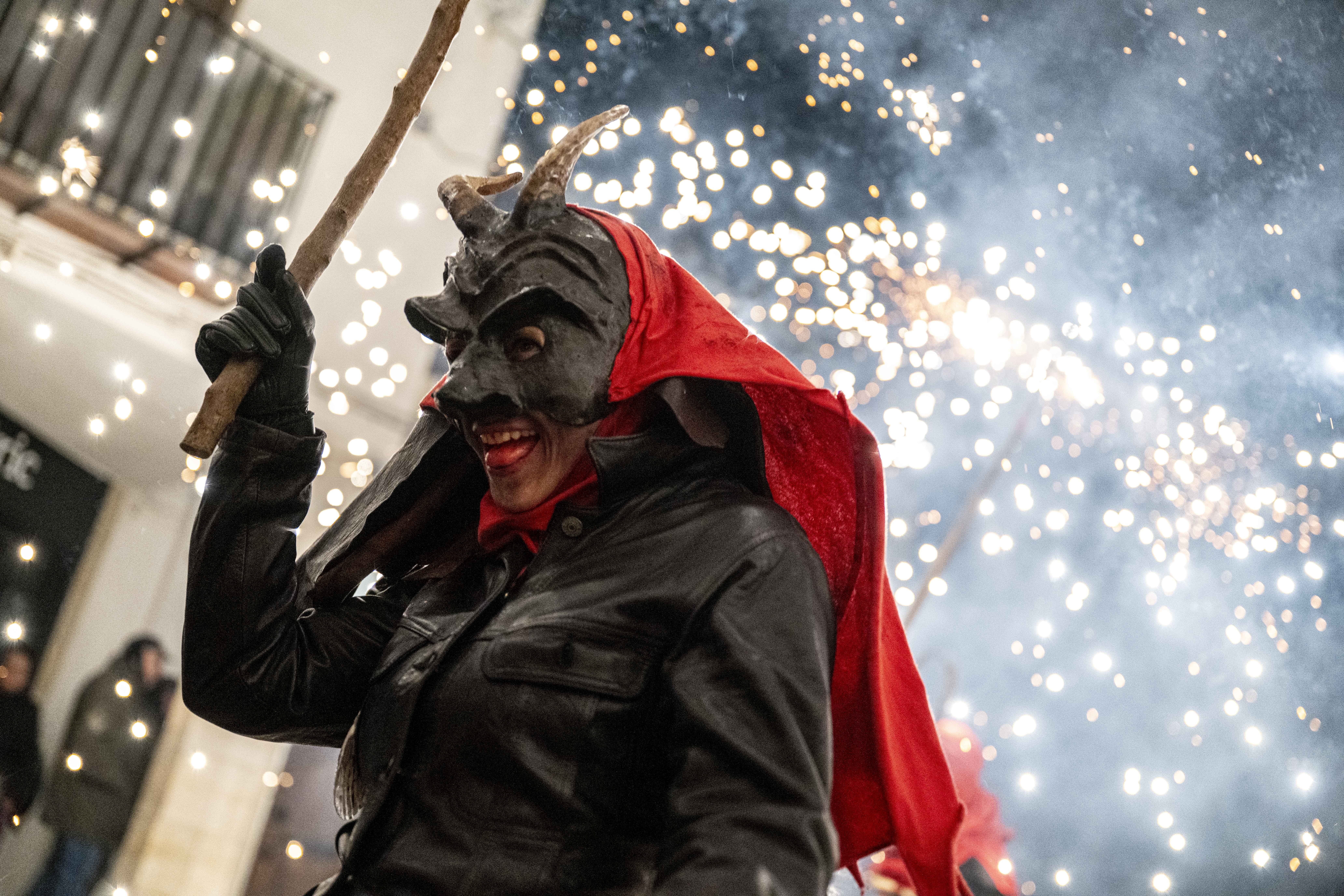 A person wearing a devil costume parades beneath exploding fireworks.