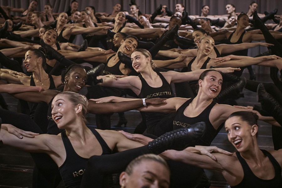 Several dozen dancers perform together, hands on one another's shoulders.
