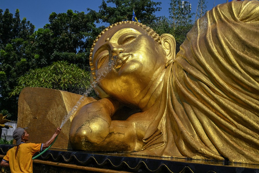 A person sprays the face of a large golden Buddha statue with a hose.