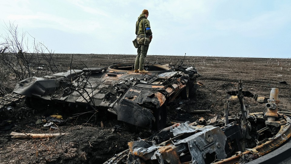 A Ukrainian soldier stands on the wreckage of a Russian tank