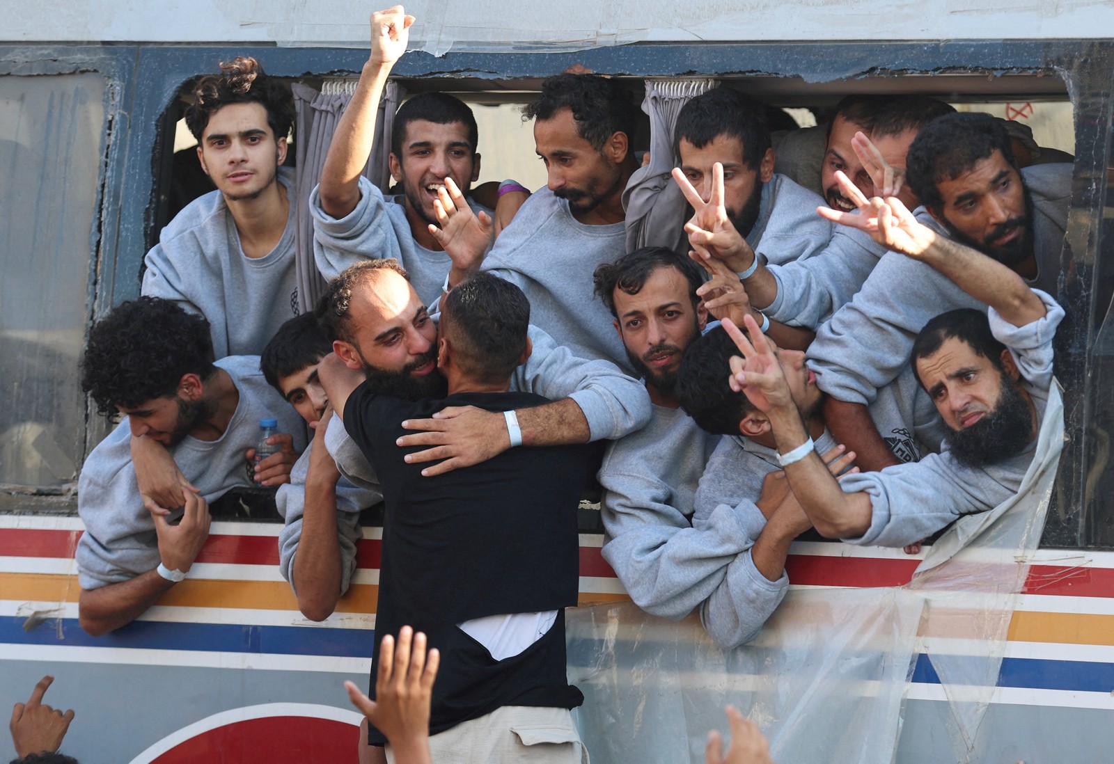 Freed Palestinian prisoners gesture through a large bus window.