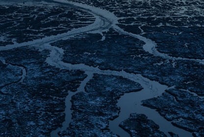 Ice masses break up a body of water in a dark landscape.