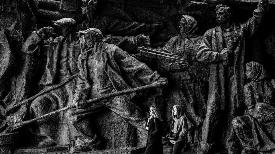 Two people walk past a large relief at the National Museum of the History of Ukraine.