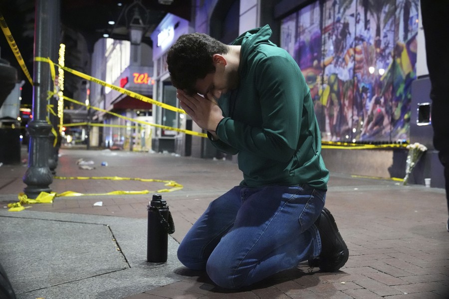 A person kneels on a sidewalk, praying, near a crime scene.