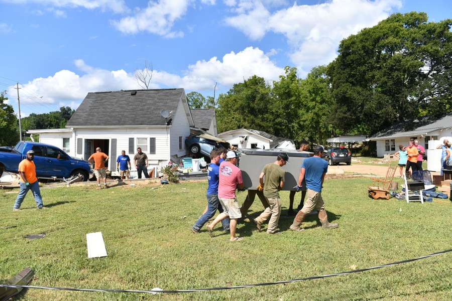 People carry a refrigerator among debris and flood-damaged homes in a neighborhood.