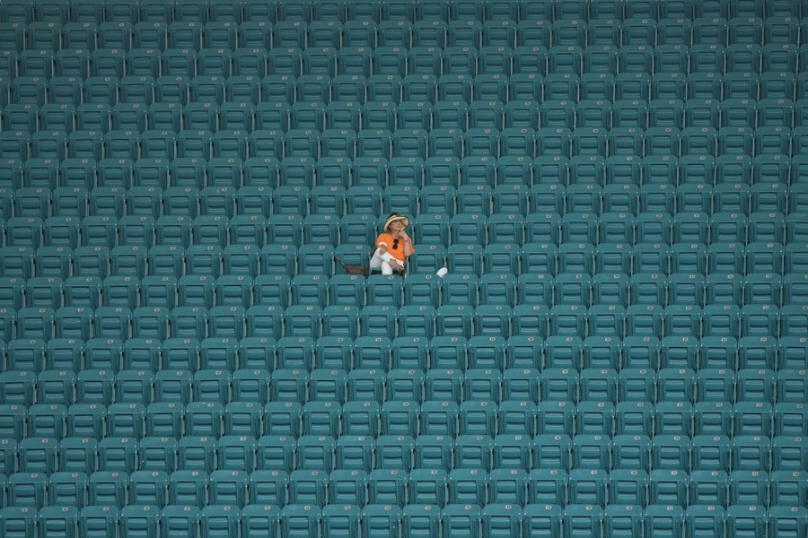A person sits alone in a large, empty section of arena seating.