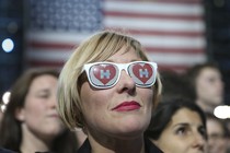 A woman wearing sunglasses with the Clinton campaign logo in front of an American flag
