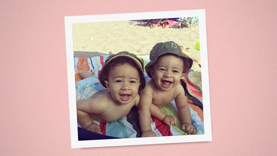 Two twin babies laying on a colorful towel at the beach