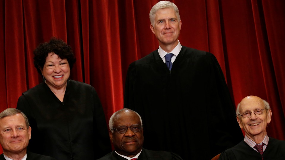 Supreme Court justices stand in front of a red backdrop. 