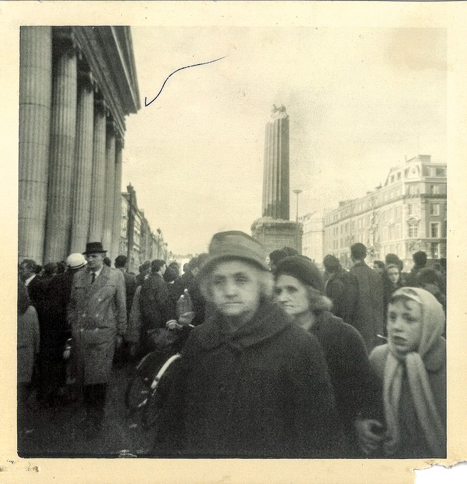 black and white photo of crowd of people with destroyed pillar and buildings behind them