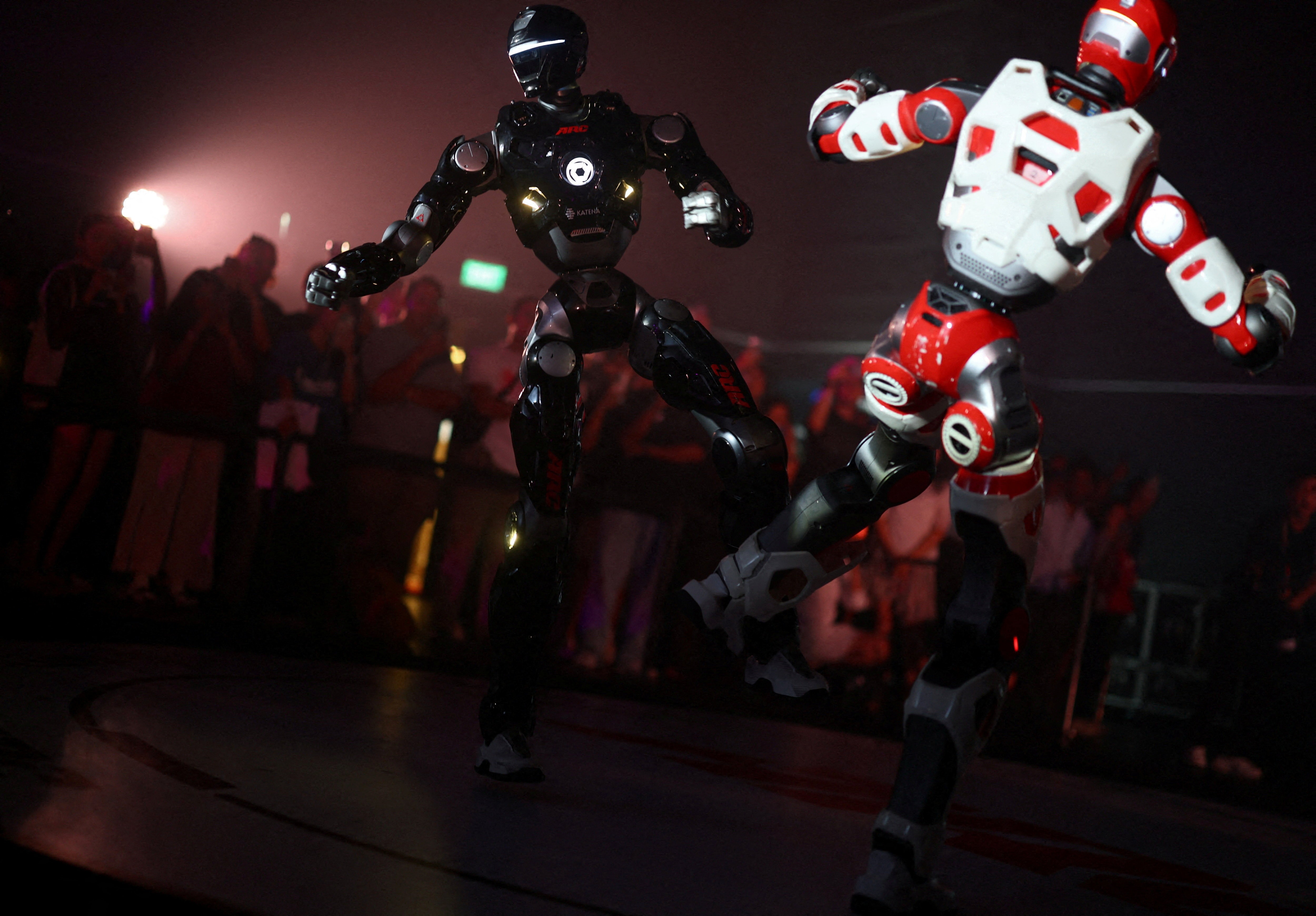 People watch as two humanoid robots fight.