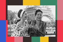 Lily Collins as Emily Cooper in "Emily in Paris" laughs with a friend while drinking champagne in front of the Eiffel Tower.