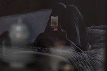 A teenager lying on a couch, looking at a cell phone.