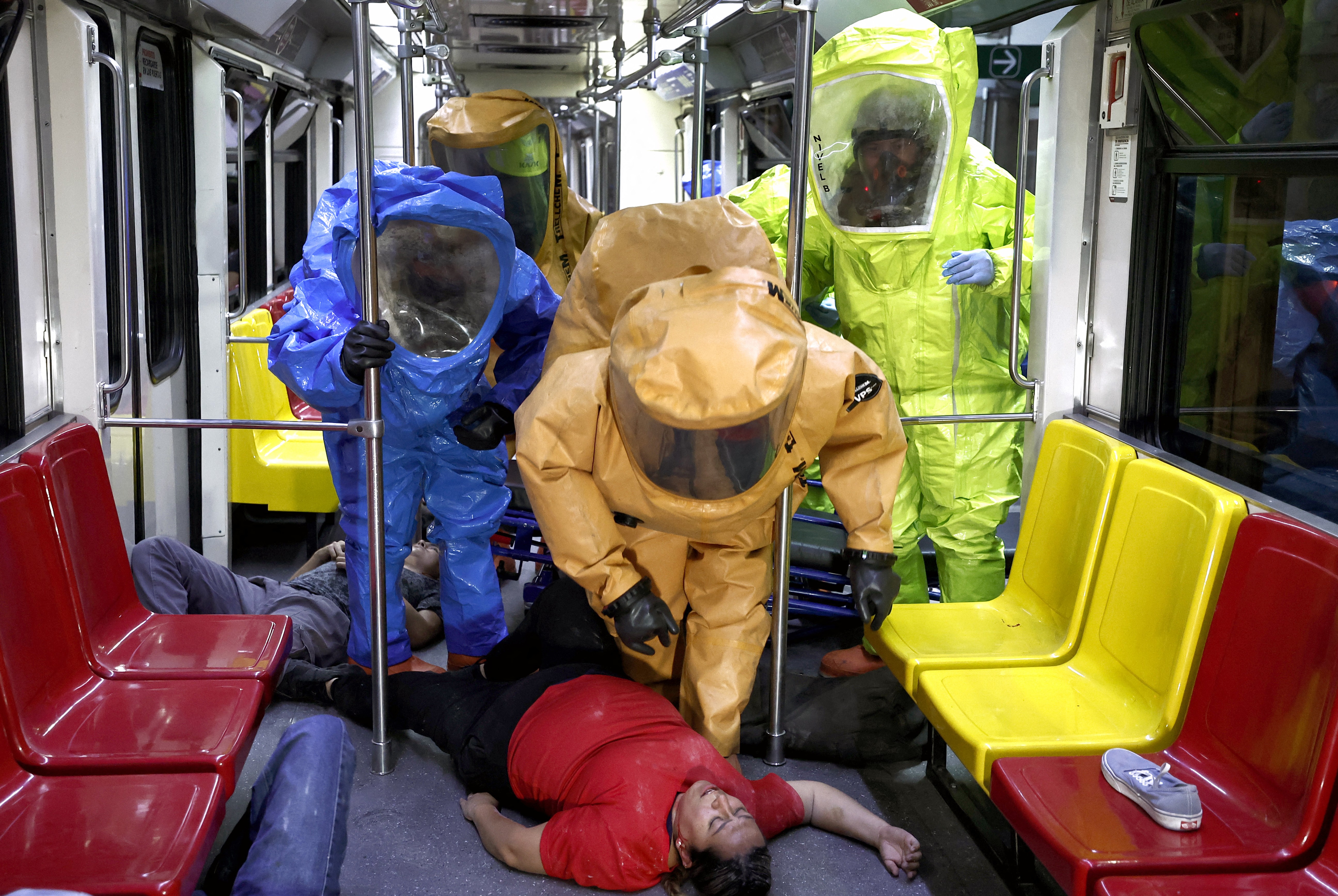 Emergency workers wearing multicolored hazmat suits, attend to people pretending to be victims of an attack on a train, during a drill.