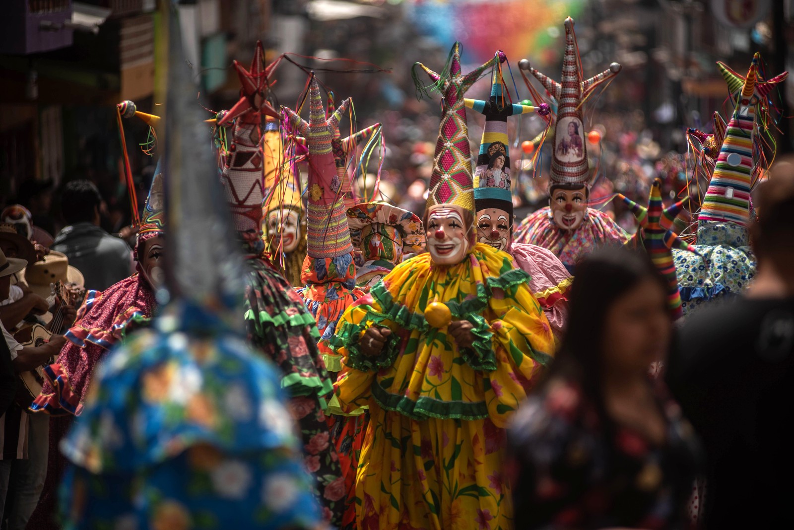 A large group of people wearing costumes resembling colorful clowns march through a street.
