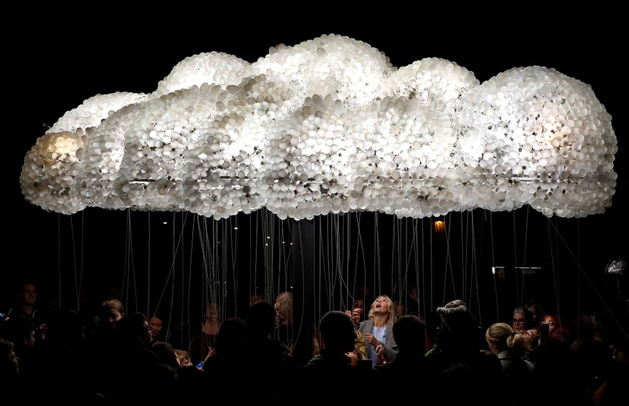 More than a dozen people look up at a cloud-shaped light installation.