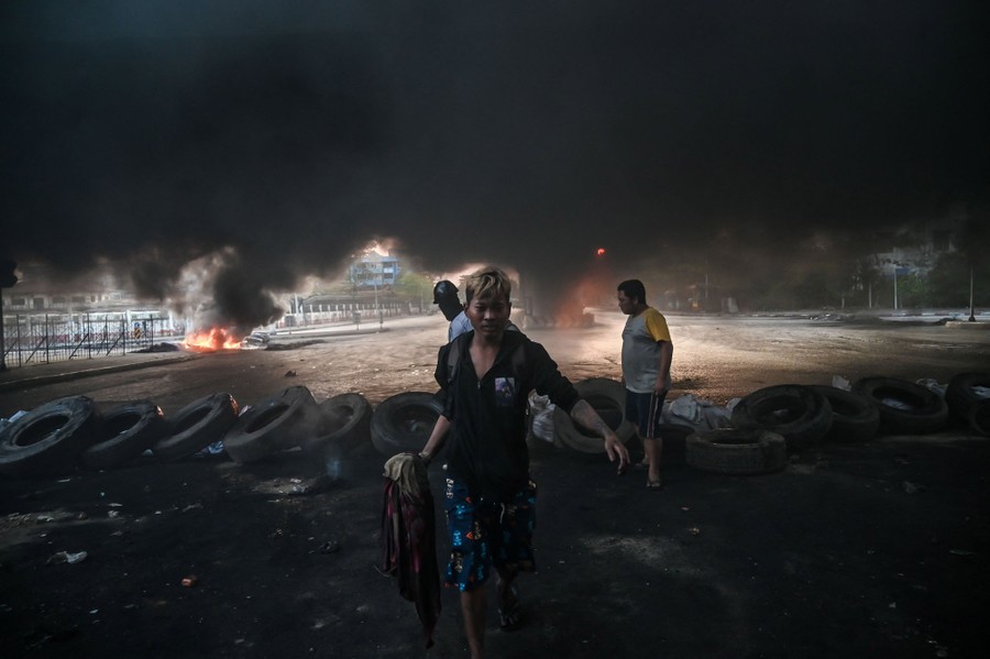 Several protesters walk on a city street under a dark cloud of smoke.