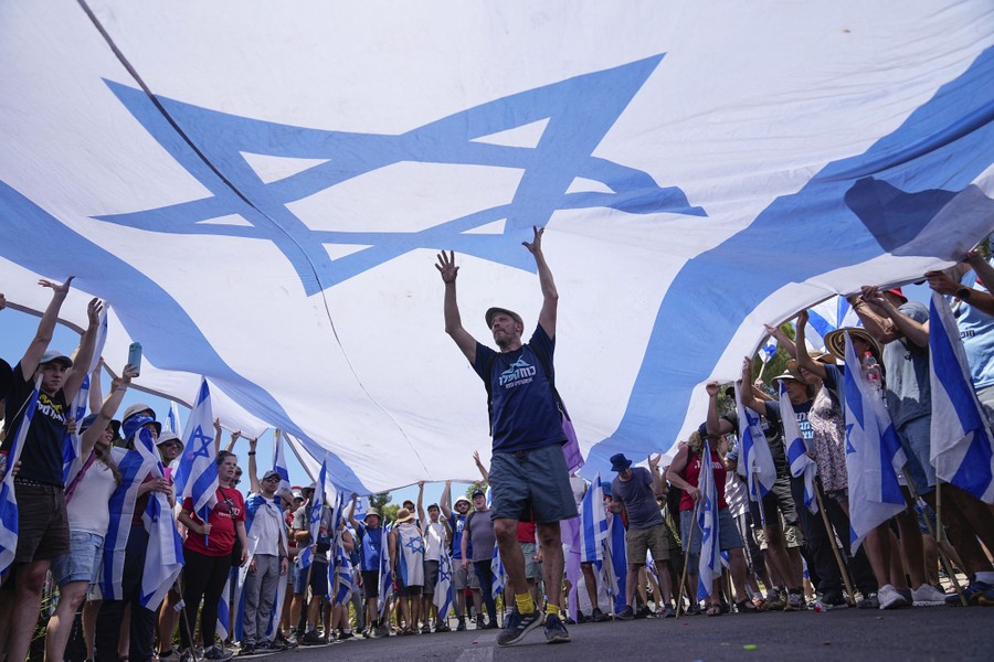 A group of protesters holds up a large Israeli flag above their heads.