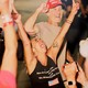 A white woman wearing a black tank top is smiling and throws her arms in the air.