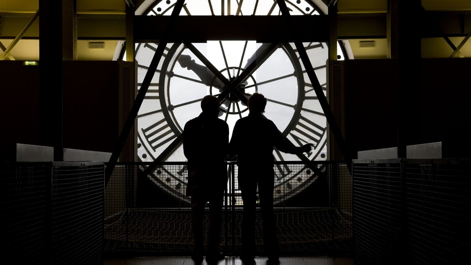 Two people are backlit while looking at a large clock