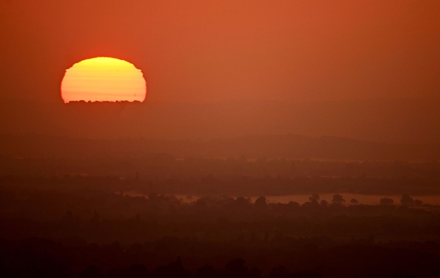 A view of the rising sun at a distance, over a gentle country landscape
