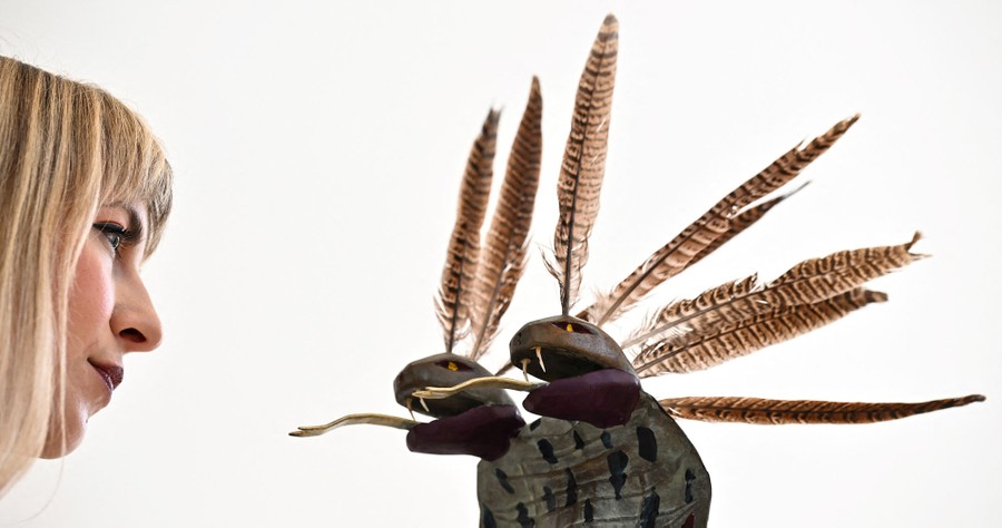 A person looks at a sculpture that resembles a two-headed snake with feathers.