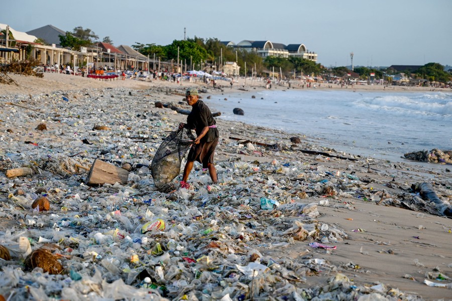 A person picks recyclable items from a broad patch of garbage strewn across a beach.