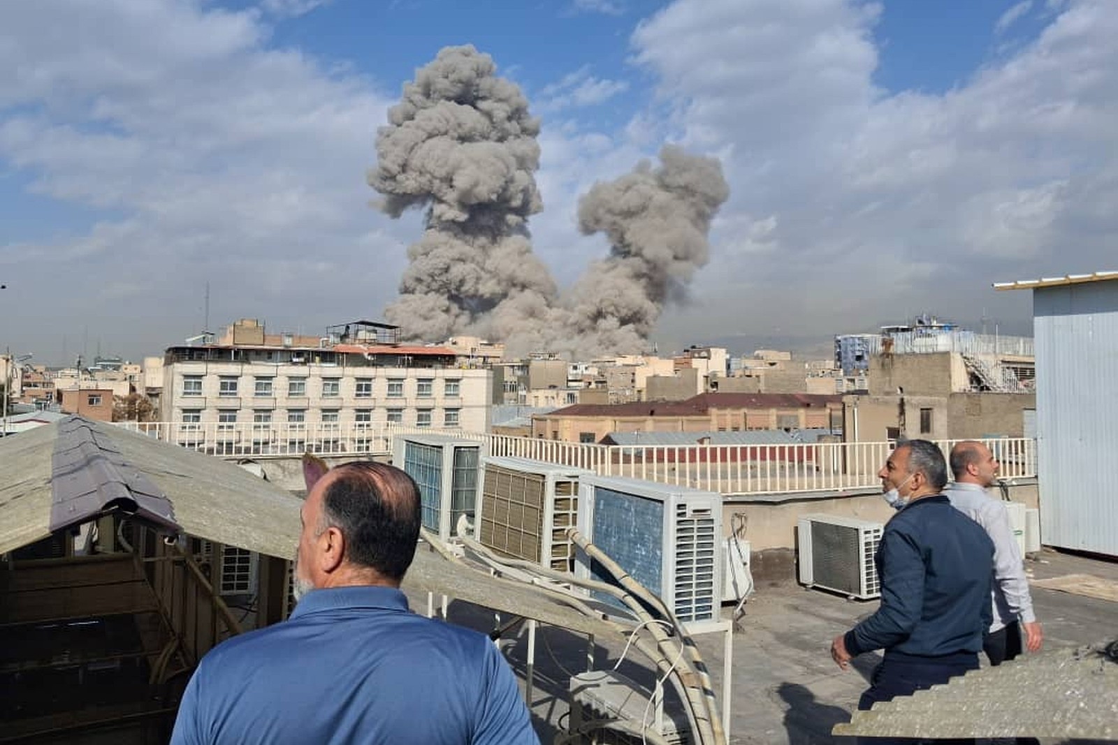 People watch as smoke and dust rises after an explosion in Tehran.