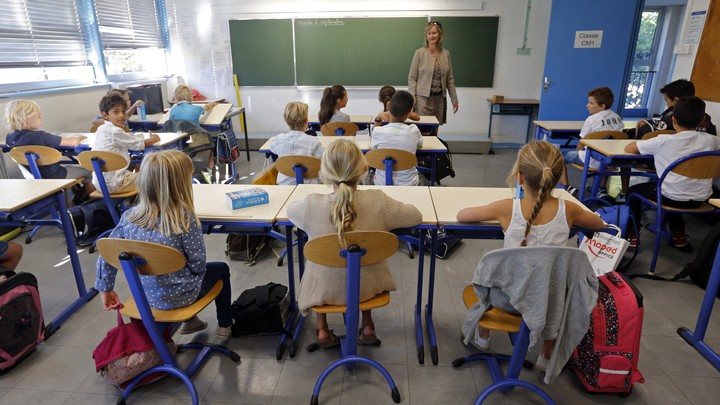 A teacher stands at the front of a classroom of students.