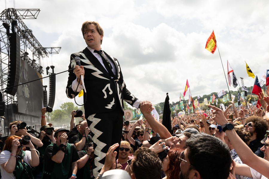 A singer performs on stage walking close to a large crowd.