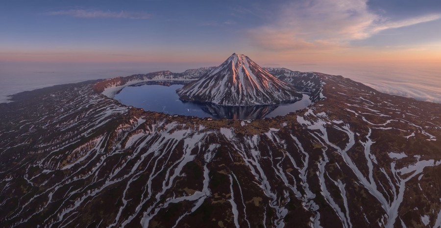 A treeless volcanic island, seen from the air, is topped by a crater lake. The lake is occupied by a smaller volcanic cone—an island on an island.