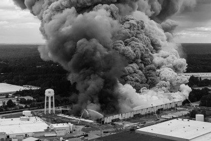 In a black-and-white photo, a large plume of smoke rises over buildings.