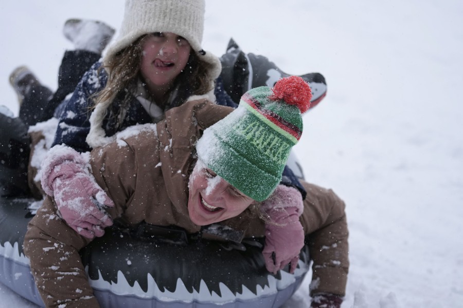 People laugh as they sled on a snow-covered hill.