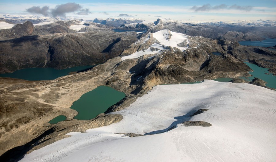 An aerial view of snow-covered mountains and water-filled valleys below.