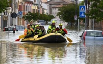 Several rescue workers paddle an inflatable boat, carrying civilians through a flooded street.